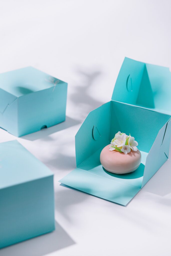 Cajas de packaging turquesa abiertas con un pastel decorado con flores